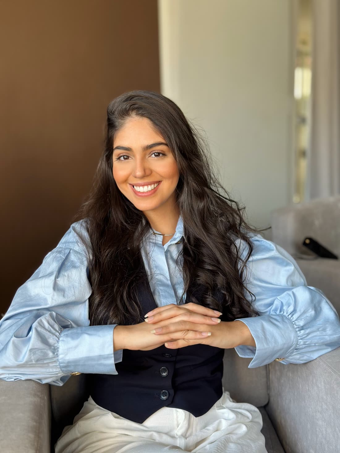 Daffine Benaion, psicóloga, sentada em uma poltrona clara, sorrindo para a câmera.